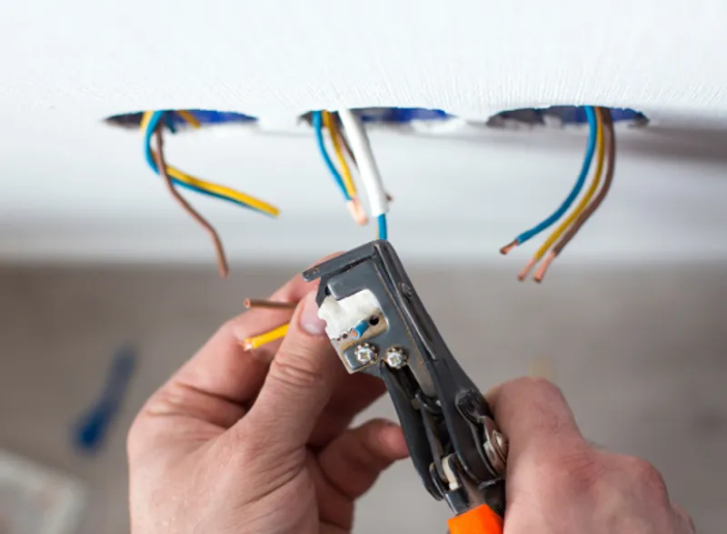 Mains d'une personne utilisant une pince à dénuder pour préparer des fils électriques pour l'installation.