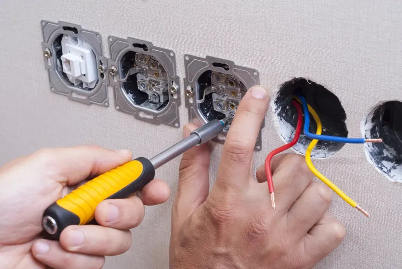Mains d'un électricien utilisant un tournevis pour installer une nouvelle prise électrique dans un mur.